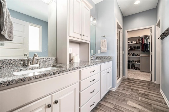 full bathroom featuring double vanity, a walk in closet, wood finish floors, and a sink