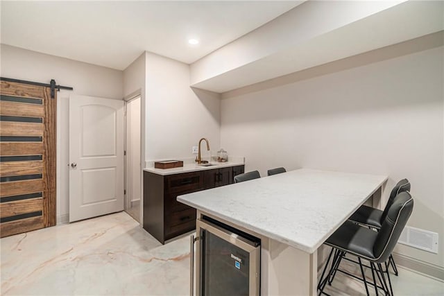 kitchen with dark brown cabinets, beverage cooler, a kitchen bar, a barn door, and a peninsula