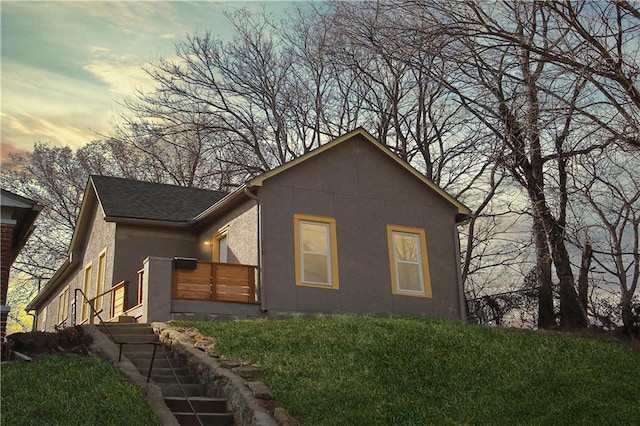 view of front of property featuring a shingled roof, a yard, and stucco siding