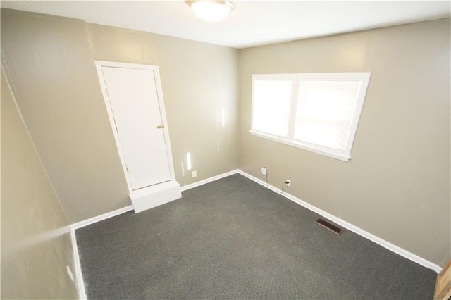 spare room featuring dark colored carpet, visible vents, and baseboards