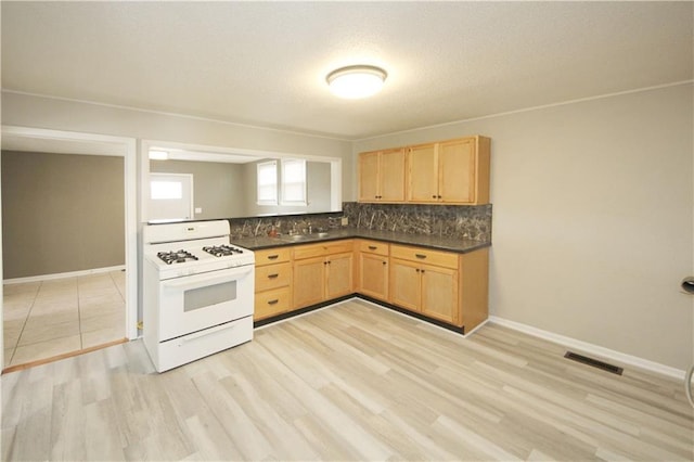 kitchen with dark countertops, visible vents, white gas stove, light brown cabinetry, and decorative backsplash