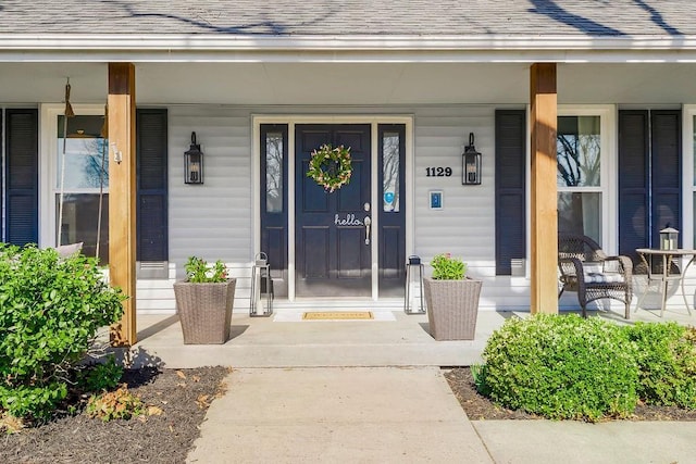 doorway to property featuring roof with shingles and covered porch