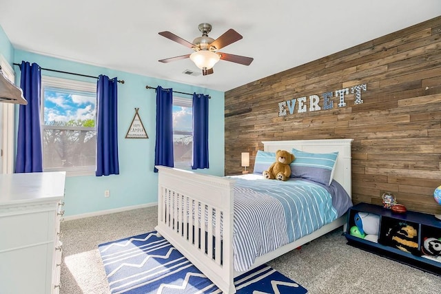 carpeted bedroom featuring visible vents, baseboards, wood walls, and a ceiling fan