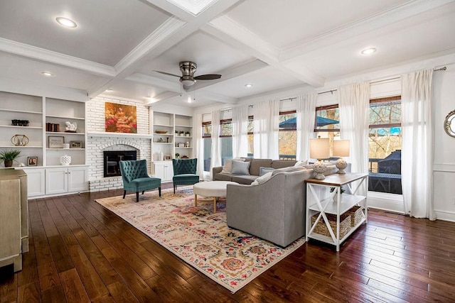 living room with ornamental molding, beam ceiling, a fireplace, a ceiling fan, and dark wood finished floors