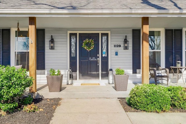 doorway to property featuring a porch and a shingled roof