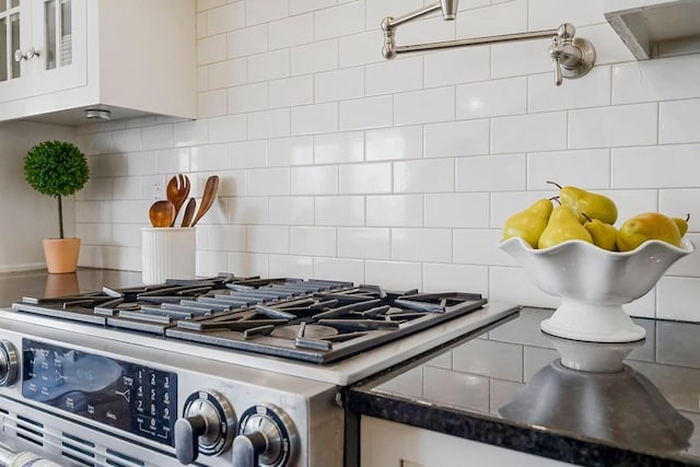 details with glass insert cabinets, stainless steel gas range oven, backsplash, and white cabinetry
