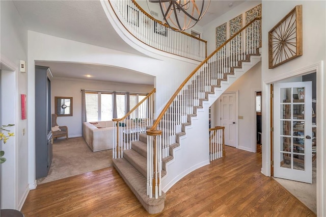 staircase featuring a notable chandelier, wood finished floors, baseboards, and a towering ceiling