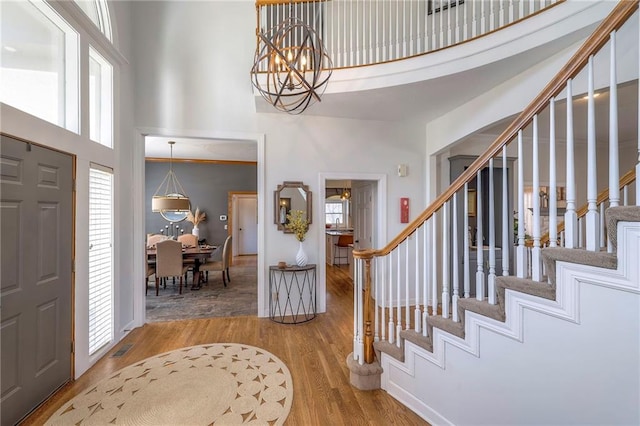 foyer entrance featuring a wealth of natural light, an inviting chandelier, wood finished floors, and a towering ceiling