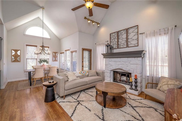 living room featuring ceiling fan with notable chandelier, a fireplace, high vaulted ceiling, and wood finished floors