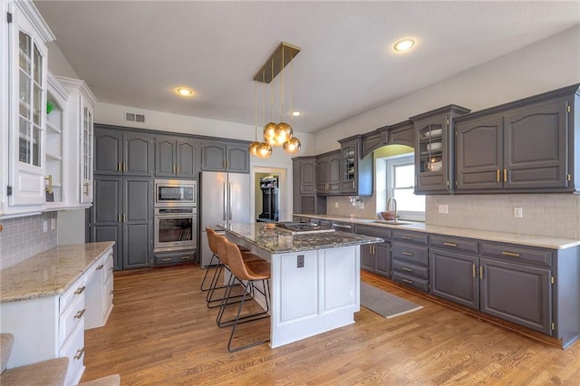 kitchen featuring visible vents, a center island, a kitchen breakfast bar, stainless steel appliances, and a sink