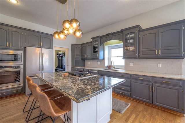 kitchen with glass insert cabinets, a kitchen bar, decorative backsplash, stainless steel appliances, and a sink