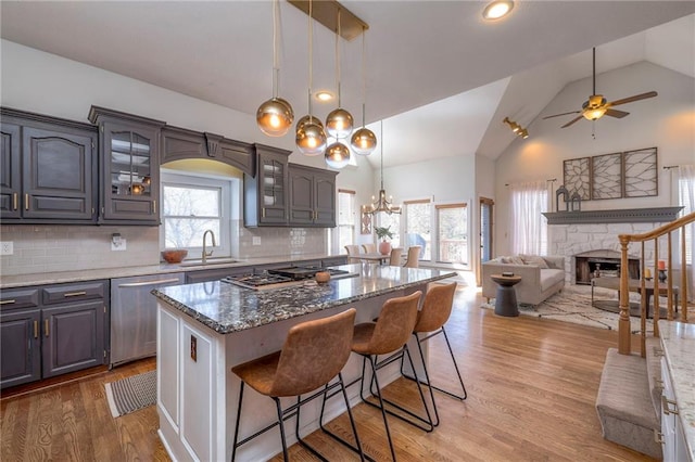 kitchen featuring a fireplace, stainless steel appliances, a sink, glass insert cabinets, and open floor plan