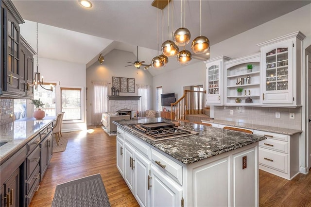 kitchen with light wood-type flooring, open shelves, white cabinetry, a stone fireplace, and stainless steel gas cooktop