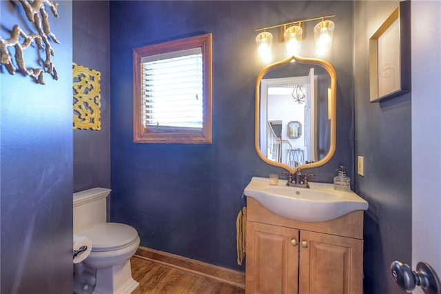 half bathroom with baseboards, toilet, wood finished floors, and vanity