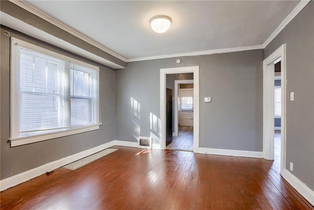 empty room with visible vents, ornamental molding, baseboards, and wood-type flooring