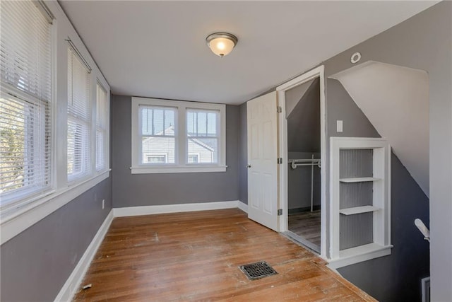 unfurnished bedroom with wood finished floors, visible vents, a closet, and baseboards