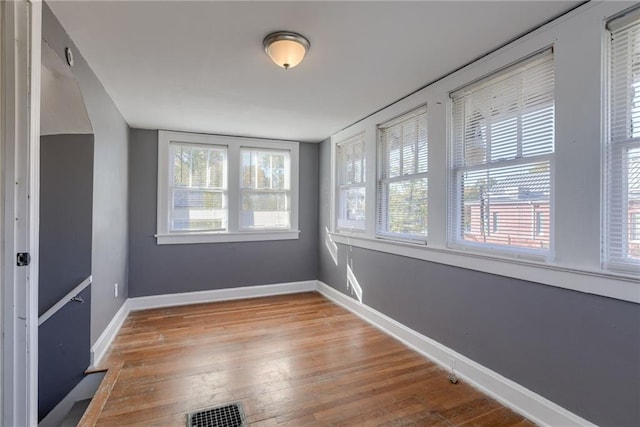 empty room with visible vents, a healthy amount of sunlight, baseboards, and wood finished floors