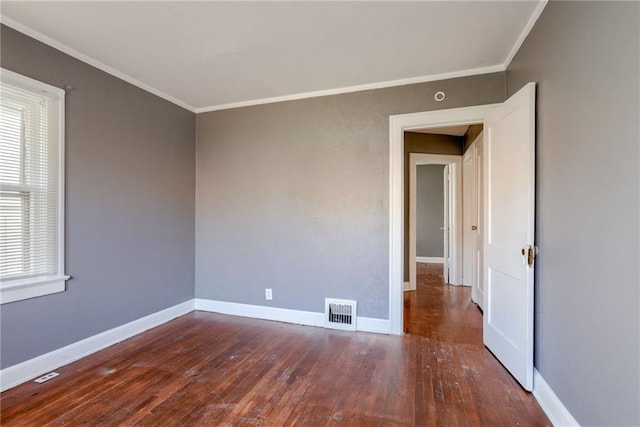 empty room featuring hardwood / wood-style floors, visible vents, baseboards, and ornamental molding