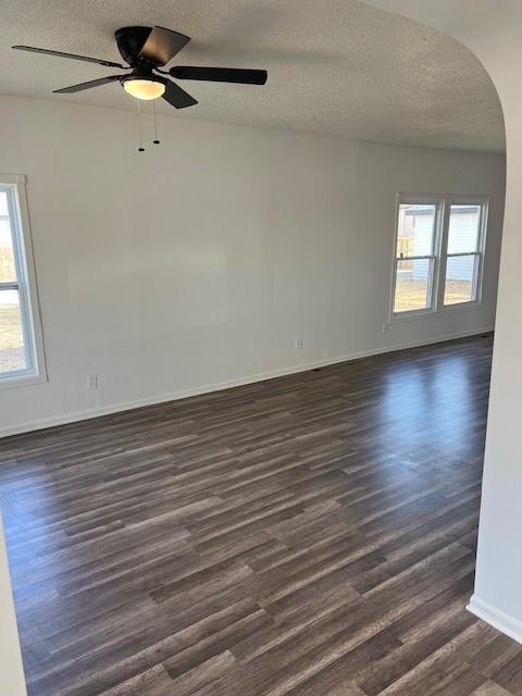 spare room featuring dark wood-type flooring, a textured ceiling, arched walkways, baseboards, and ceiling fan