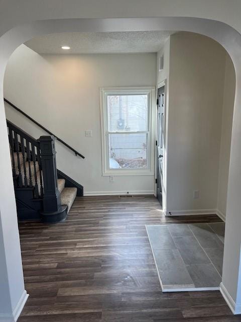 foyer entrance featuring baseboards, stairway, arched walkways, dark wood-style floors, and a textured ceiling