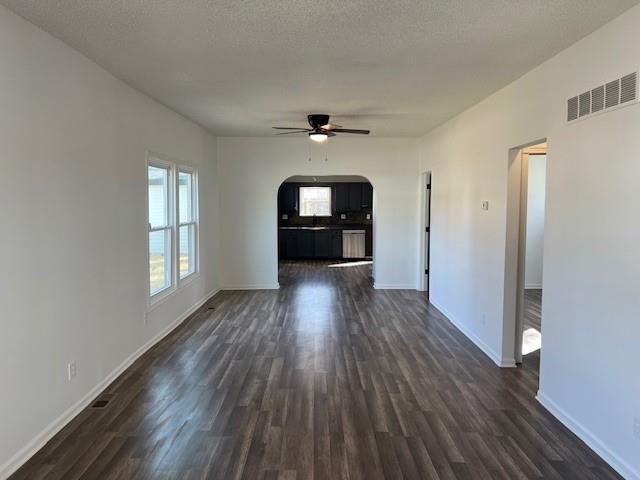 unfurnished living room with dark wood-style floors, baseboards, visible vents, arched walkways, and ceiling fan