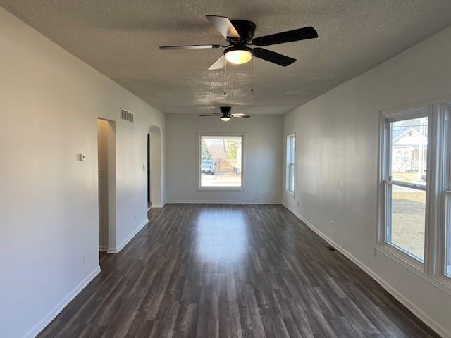 spare room with baseboards, visible vents, dark wood finished floors, arched walkways, and a textured ceiling