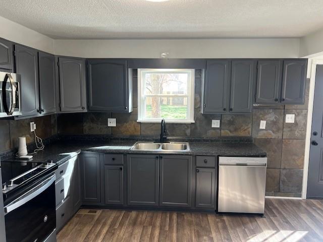 kitchen with dark countertops, gray cabinets, appliances with stainless steel finishes, and a sink