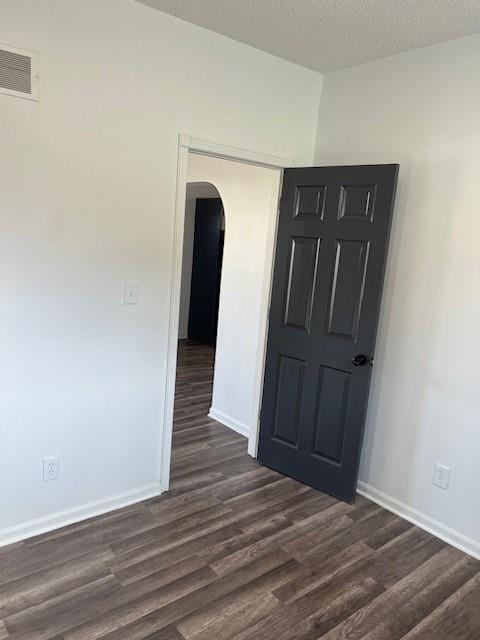 empty room with visible vents, baseboards, dark wood finished floors, arched walkways, and a textured ceiling