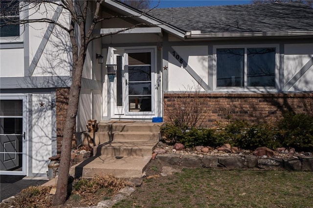 entrance to property featuring a shingled roof and stucco siding