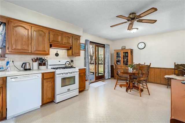 kitchen with brown cabinetry, wainscoting, white appliances, and light countertops