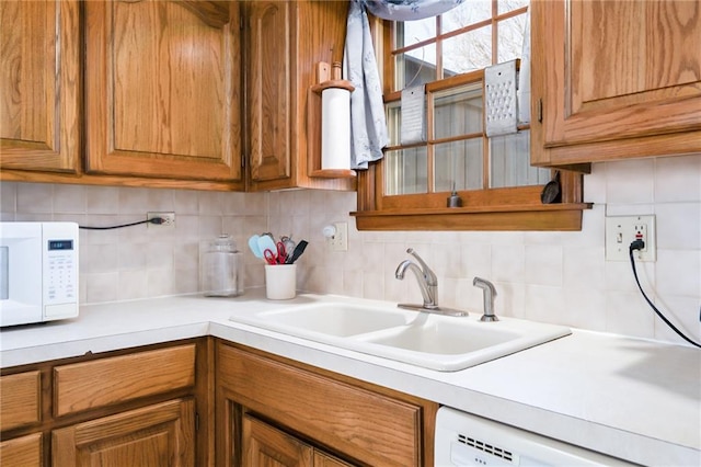 kitchen with tasteful backsplash, light countertops, brown cabinetry, white appliances, and a sink