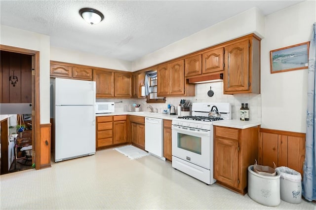 kitchen with white appliances, light countertops, a wainscoted wall, and brown cabinets