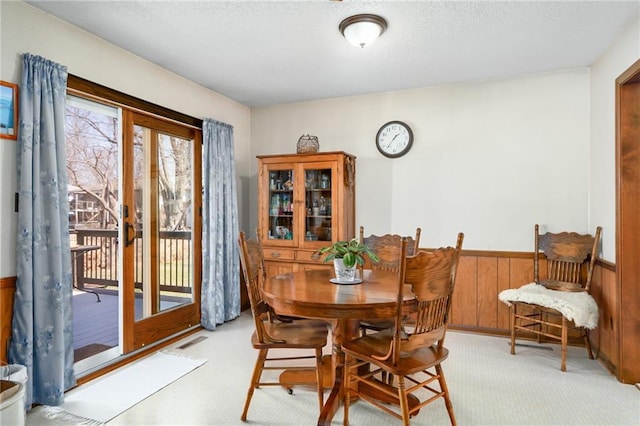 dining room with visible vents, light carpet, a textured ceiling, wooden walls, and wainscoting