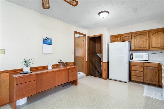 interior space featuring light countertops, brown cabinetry, white appliances, a textured ceiling, and a ceiling fan