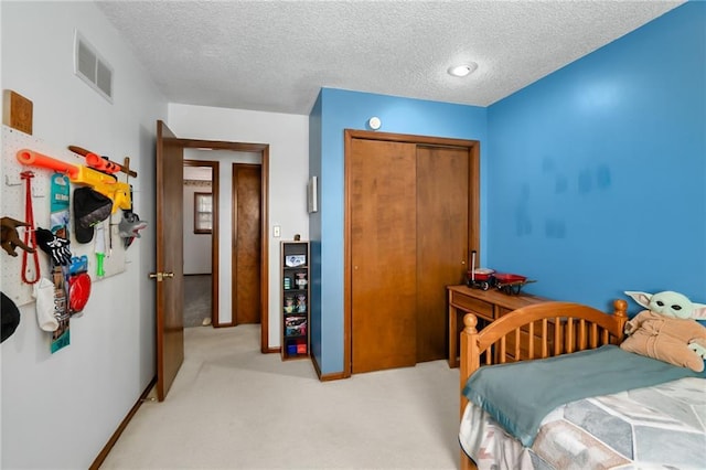 bedroom featuring a closet, visible vents, light colored carpet, and a textured ceiling