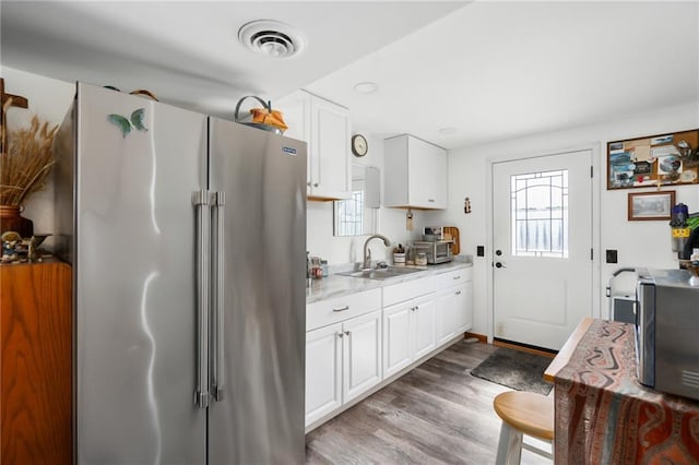 kitchen with visible vents, appliances with stainless steel finishes, wood finished floors, white cabinetry, and a sink