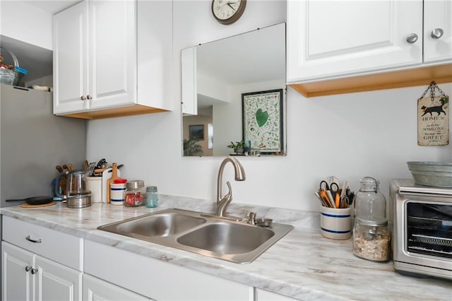 kitchen featuring a toaster, white cabinetry, light countertops, and a sink