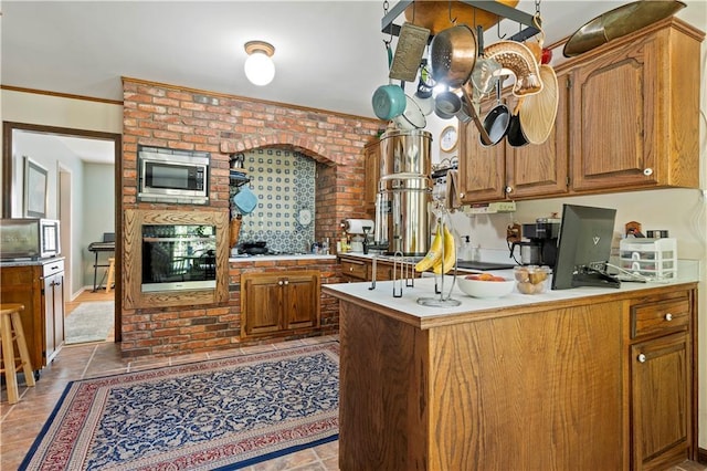 kitchen with brown cabinetry, stainless steel microwave, light countertops, and light tile patterned flooring