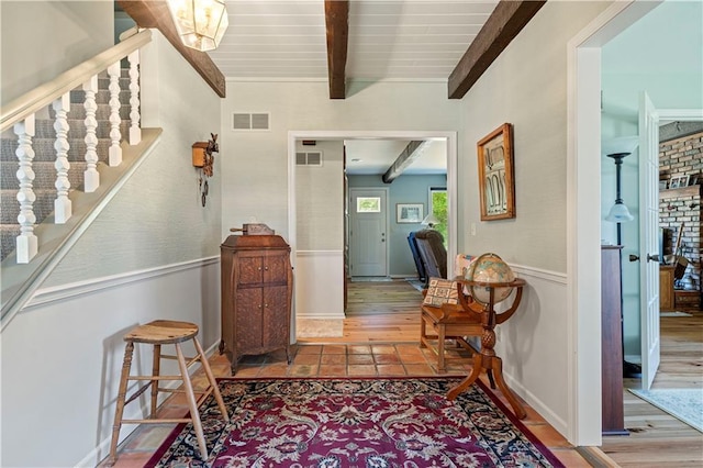 foyer entrance with beamed ceiling, a wainscoted wall, stairs, and visible vents