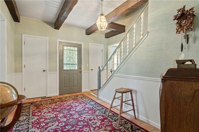 foyer with stairs, a wainscoted wall, beam ceiling, and light tile patterned floors