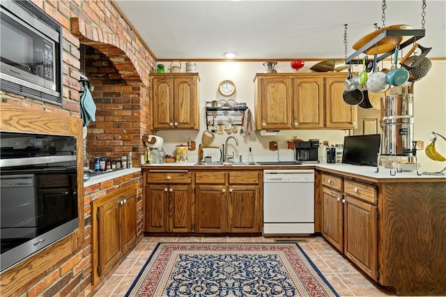 kitchen featuring white dishwasher, a sink, brown cabinetry, oven, and stainless steel microwave