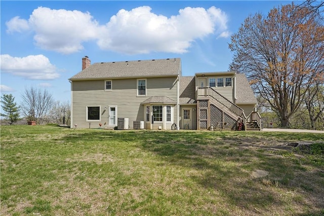 rear view of property with a chimney, a yard, central AC, and stairs