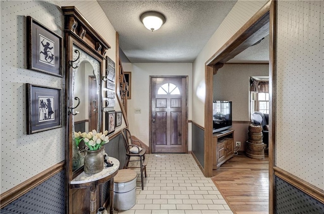 foyer entrance featuring wallpapered walls, wainscoting, light wood finished floors, and a textured ceiling