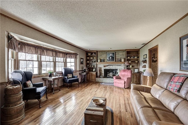 living area featuring built in shelves, ornamental molding, hardwood / wood-style floors, a fireplace, and a textured ceiling