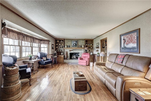 living room with a stone fireplace, light wood-style flooring, ornamental molding, and a textured ceiling