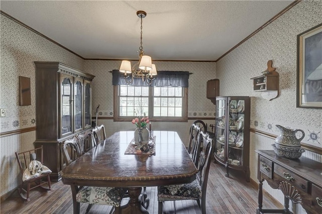 dining room featuring wallpapered walls, ornamental molding, wainscoting, wood finished floors, and a textured ceiling