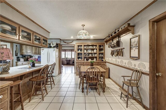 dining area with light tile patterned floors, a wainscoted wall, a textured ceiling, and crown molding