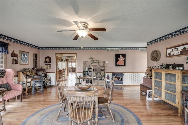 dining space featuring a ceiling fan, wood finished floors, visible vents, and a textured ceiling