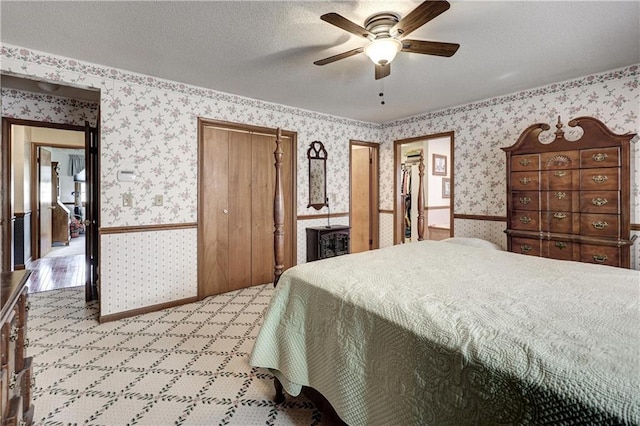 bedroom featuring a textured ceiling, a closet, wainscoting, wallpapered walls, and ceiling fan