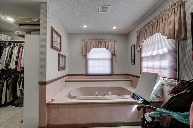 bathroom featuring a spacious closet, a bath, visible vents, and a textured ceiling